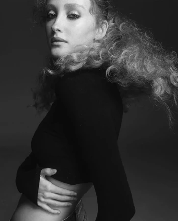 Monochrome portrait of a woman with voluminous curly hair wearing a dark fitted long-sleeve top by make-up artist Nicole Pinky Thompson